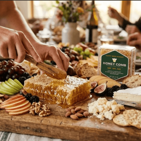 Hand cutting fresh Happy Bees Market raw honeycomb with a wooden spoon on a large party charcuterie board with brie, crackers, sliced apples, figs, grapes, and nuts.