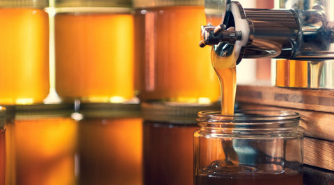 Raw Arizona B-Grade Honey dripping from a wooden honey dipper into a glass jar — unfiltered, local, and rich in natural pollen from Happy Bees Market.