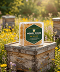 Happy Bees Market 12 oz packaged raw honeycomb resting on a rustic wooden beehive box in a blooming wildflower apiary field.